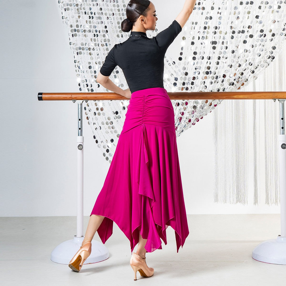 Fuchsia ballroom dance skirt with ruched hip yoke and pointed hem, back view at the barre
