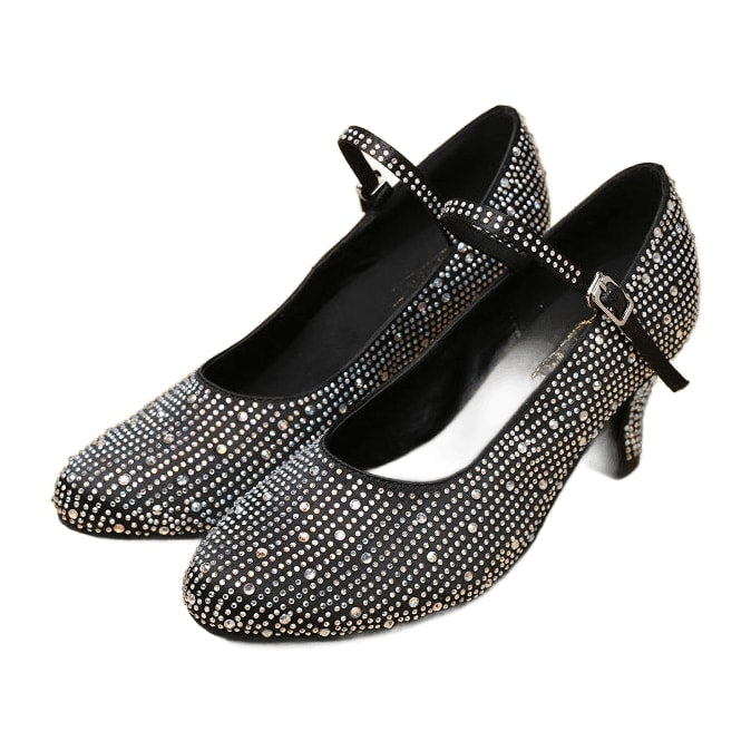 pair of black rhinestone-embellished ballroom dance shoes for women, closed-toe with ankle strap on wood floor