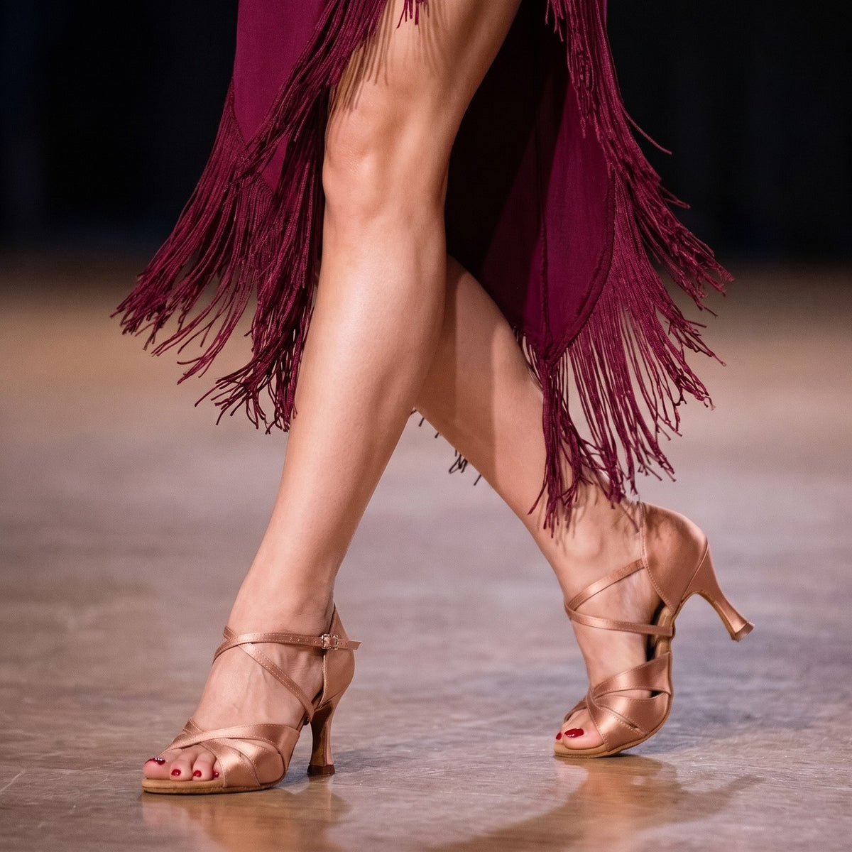Woman wearing nude satin criss-cross open toe latin salsa dance shoes on a ballroom floor