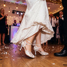 Bride dancing in white satin AB rhinestone closed toe ballroom wedding shoes on a wood floor under festoon lights