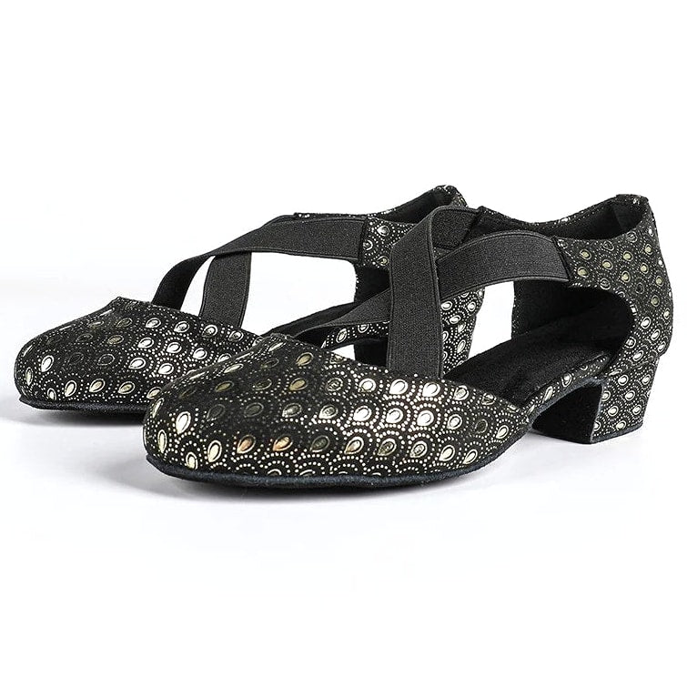 Black ballroom dance shoes pair with metallic gold peacock-eye print, closed round toe and crossed elastic straps on a low block heel
